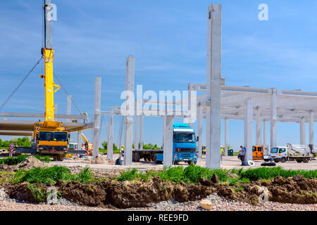 Mobilkran ist die Montage sehr große Betonskelett des gewerblichen Gebäude. Landschaft in städtischen Gebiet mit Maschinen verwandeln, Menschen arbeiten. Anzeigen o Stockfoto