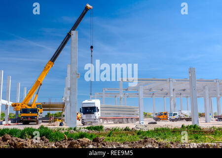 Mobilkran ist die Montage sehr große Betonskelett des gewerblichen Gebäude. Landschaft in städtischen Gebiet mit Maschinen verwandeln, Menschen arbeiten. Anzeigen o Stockfoto