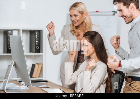 Happy Business Mentor mit lächelnden jungen Kollegen schütteln Fäuste und suchen Sie auf dem Desktop Computer im Büro Stockfoto