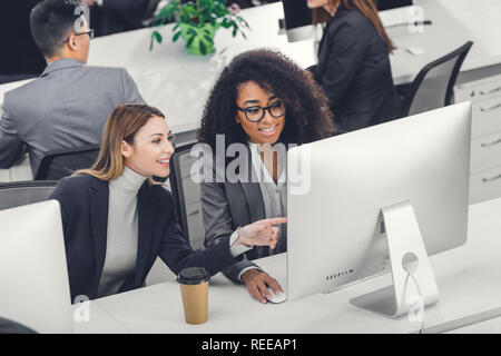 Hohe Betrachtungswinkel von lächelnden multiethnischen Unternehmerinnen mit Desktop-PC im Büro Stockfoto