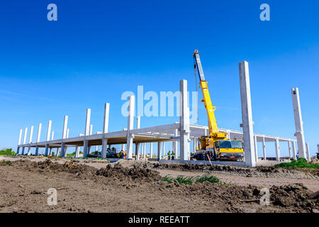 Mobilkran ist die Montage sehr große Betonskelett des gewerblichen Gebäude. Landschaft in städtischen Gebiet mit Maschinen verwandeln, Menschen arbeiten. Anzeigen o Stockfoto