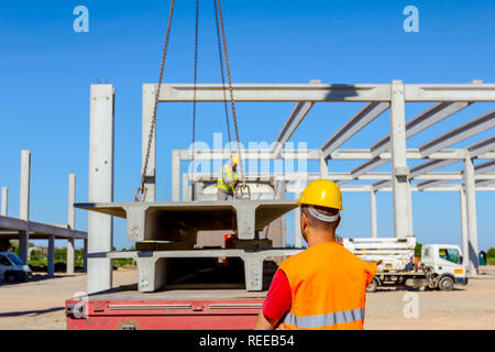 Ansicht von hinten auf Bauarbeiter mit Warnweste und gelben Helm überwachung entladen konkrete Balken aus LKW-Anhänger. Stockfoto