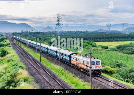 Ehrfürchtige Nahansicht des Motors der indischen Eisenbahn, die auf der Strecke läuft, geht zum Horizont in grüner Landschaft unter blauem Himmel mit Wolken. Stockfoto
