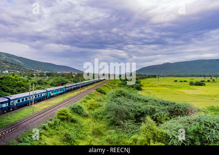 Tolle Aussicht auf indische Eisenbahn läuft auf der Strecke geht zum Horizont in grüner Landschaft unter blauem Himmel mit Wolken. Stockfoto