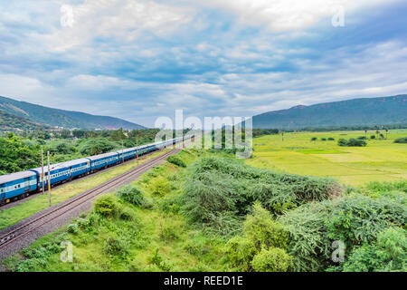 Tolle Aussicht auf indische Eisenbahn läuft auf der Strecke geht zum Horizont in grüner Landschaft unter blauem Himmel mit Wolken. Stockfoto