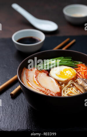 Asiatische Ramen-Suppe mit Huhn, Ei, Karotten, grüne Zwiebeln auf einem dunklen Hintergrund. Stockfoto