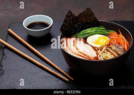 Asiatische Ramen-Suppe mit Huhn, Ei, Karotten, grüne Zwiebeln auf einem dunklen Hintergrund. Stockfoto