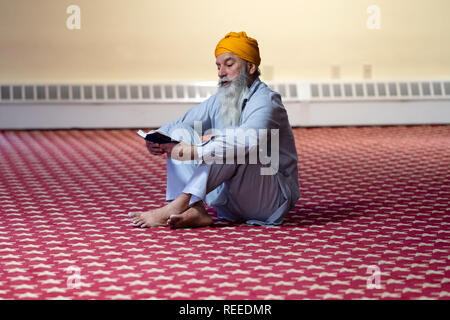 Ein frommer Sikh mann Lesung sein Gebet Buch an einem Tempel in Richmond Hill, Queens, New York City. Stockfoto