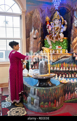 Ein im mittleren Alter Hindu devotee gießt Milch über einen Lingam in der Nähe einer Statue von Shiva an einem Tempel in RichmondHill, Queens, New York City. Stockfoto