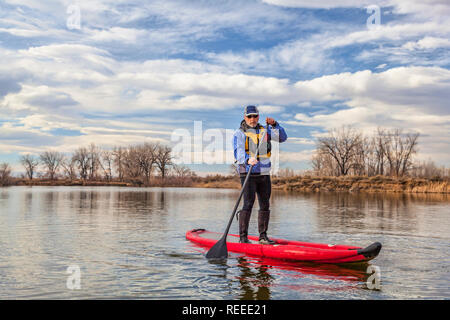 Älterer Mann ist das Paddeln eine aufblasbare Stand up paddleboard auf einem See im Herbst oder Winter Landschaft in Colorado Stockfoto
