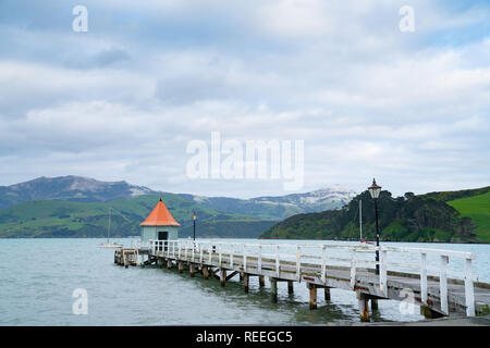 Daly's Wharf oder Akaroa Bootsanleger im Hafen von Akaroa mit Schuppen und Orangefarbene runde Kegeldach am Ende Stockfoto