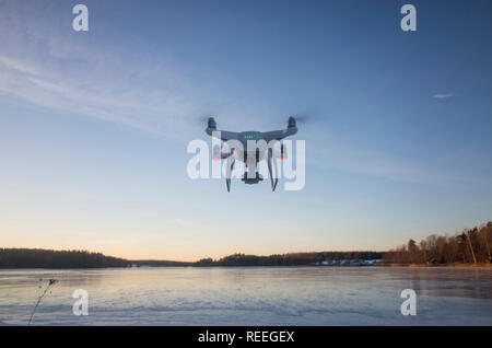 Weiß Drohne fliegen in der Luft auf Eis See in Schweden Skandinavien Europa auf kalten Winterabend. Schön draußen bei Sonnenuntergang. Natur, Landschaft und blauer Himmel. Stockfoto
