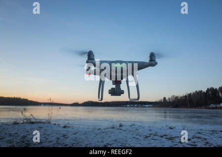 Weiß Drohne fliegen in der Luft auf Eis See in Schweden Skandinavien Europa auf kalten Winterabend. Schön draußen bei Sonnenuntergang. Natur, Landschaft und blauer Himmel. Stockfoto