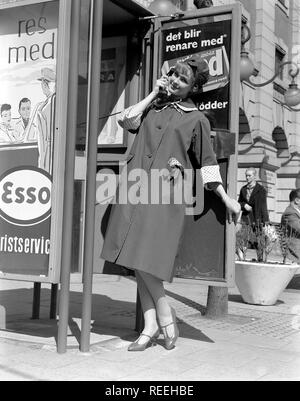 Mode in den 50er Jahren. Eine junge Frau trägt eine typische 50er Mantel. Sie posiert in der Outfit während sie vorgibt, auf ein Telefon in einer Telefonzelle zu sprechen. Schweden 1950. Foto Kristoffersson Ref315 A-7 Stockfoto