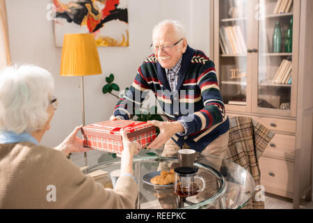 Portrait von Happy senior Paar ihre Weihnachtsgeschenke austauschen über Tabelle zu Hause sitzen Stockfoto