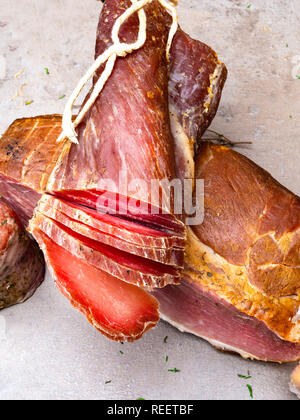 Geräucherter Schinken, jerky beef Corned auf Tisch mit Knoblauch, Kräutern auf steinernen Tisch Stockfoto