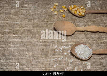 Mais und Reis in hölzerne Löffel auf dem Tisch sind bereit für die Zubereitung von Speisen Stockfoto