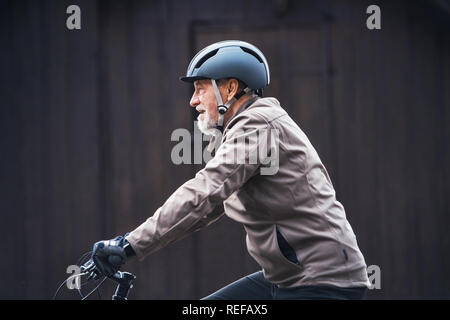 Active Senior Mann mit Fahrrad Helm Radfahren im Freien againts dunklen Hintergrund. Stockfoto