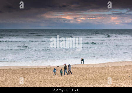 Schöne pastell Farben in den Himmel, wie die Sonne über Menschen zu Fuß entlang Fistral Beach in Newquay Cornwall. Stockfoto