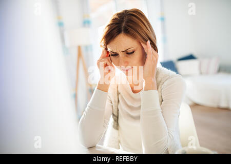 Eine junge Frau in Schmerzen sitzen drinnen, Arbeiten im Home Office. Stockfoto
