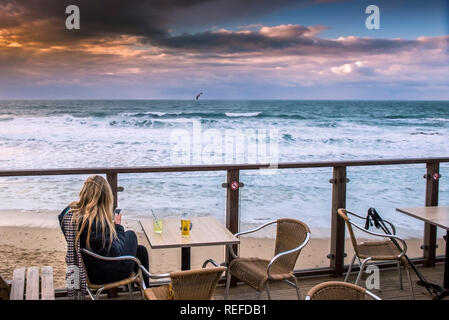 Eine Frau, die entspannend und einen spektakulären Sonnenuntergang Gebäude auf den Fistral Beach in Newquay Cornwall. Stockfoto