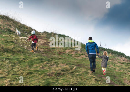 Ein Vater mit seinen beiden Kindern und ihrem Hund gehen auf einem Hügel in der Landschaft. Stockfoto