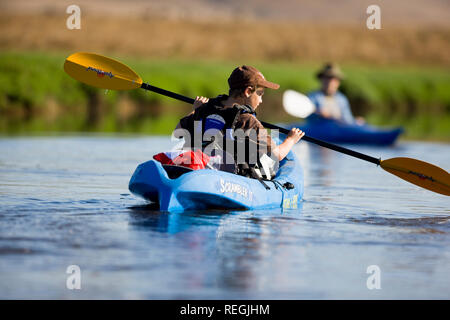 Junge Paddeln mit ein Ruder an einem Fluss in einem blauen Kajak. Stockfoto