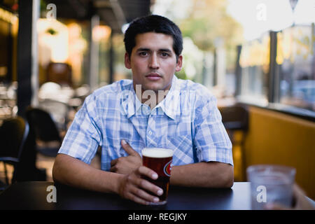 Porträt eines jungen erwachsenen Mann an der Bar mit einem Bier sitzen. Stockfoto