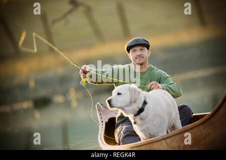 Jungen Erwachsenen Mann mit seinem Hund in einem Kanu angeln an einem See. Stockfoto