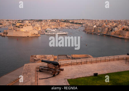 Eine einsame Kanone auf die ehrenkompanie Batterie über den Grand Harbour und Städte Senglea und Paola von Upper Barrakka Gardens, Valletta, Malta zeigt. Stockfoto