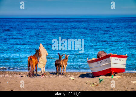 Oued Laou, Chefchaouen, Marokko - November 3, 2018: Ein junger Mann im traditionellen marokkanischen Kleidung geht seinen Esel am Strand von Oued Laou. Spaß Stockfoto