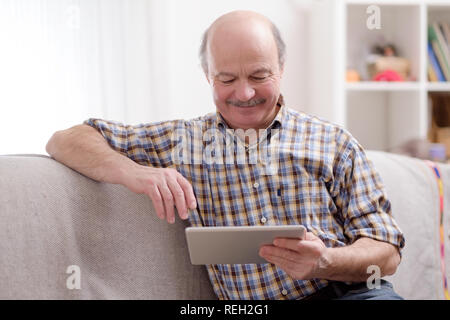 Ältere Menschen mit Tablette zu Hause sitzen. Stockfoto
