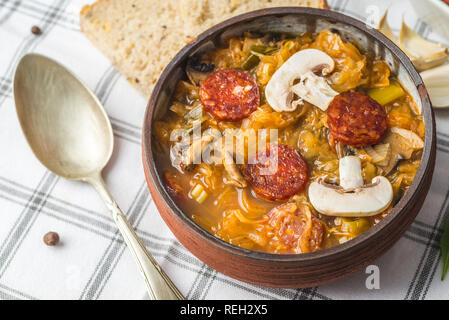 Slowakische Weihnachten nationalen Kohlsuppe in kleinen schwarzen Topf mit Wurst auf der Tischdecke Hintergrund. Stockfoto