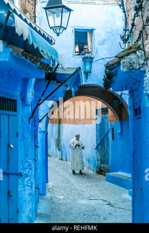 Chefchaouen, Morocco-November 4, 2018: Ein alter Mann in traditionellen marokkanischen gekleidet geht eine Gasse mit einem Bogen von der Medina von Chefchaoen Stockfoto