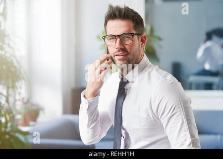 Close-up Portraitfotos der stattlichen Geschäftsmann mit Hemd und Krawatte im Büro sitzt und spricht mit jemand auf seinem Handy. Stockfoto