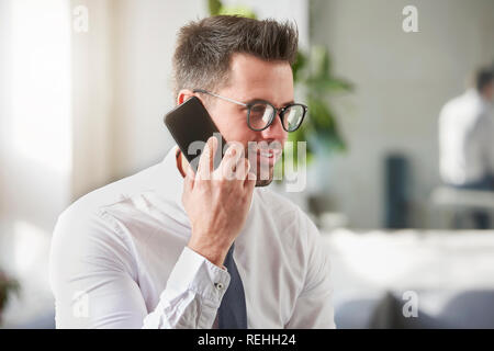 Close-up Portraitfotos der stattlichen Geschäftsmann mit Hemd und Krawatte im Büro sitzt und spricht mit jemand auf seinem Handy. Stockfoto