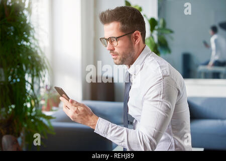 Portraitfotos der Geschäftsmann mit seinem Handy und Sms, während im Büro zu sitzen. Stockfoto