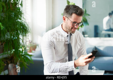 Portraitfotos der Geschäftsmann mit seinem Handy und Sms, während im Büro zu sitzen. Stockfoto