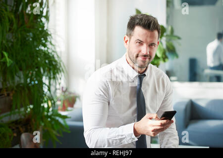 Portraitfotos der Geschäftsmann mit seinem Handy und Sms, während im Büro zu sitzen. Stockfoto