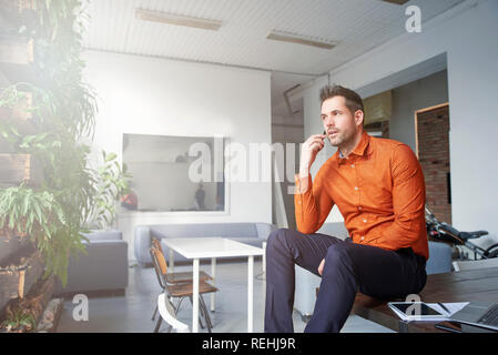 Porträts der Geschäftsmann holding Handy in der Hand und einen Anruf beim Sitzen am Schreibtisch. Stockfoto