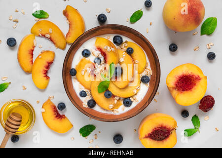 Joghurt mit Pfirsichen, Hafer, Blaubeeren, Honig und Minze in eine Schüssel für gesundes Frühstück auf weißem Hintergrund. top View Stockfoto