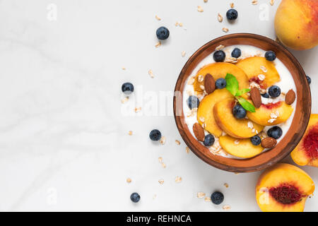 Schüssel von Hafer mit griechischem Joghurt, frische Pfirsiche, Blaubeeren und Minze auf weißem Marmor tisch für gesundes Frühstück. Ansicht von oben mit der Kopie Raum Stockfoto