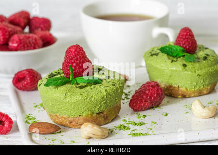 Green Matcha und Banane vegan raw Käsekuchen mit Himbeeren, Minze, Nüssen und Kaffee Tasse über weiße Holztisch. Gesunde leckeres Frühstück. nach oben vi. Stockfoto