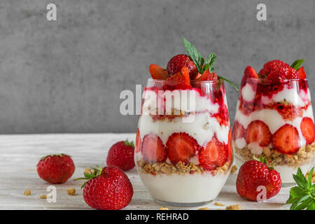 Gesunde Erdbeer Joghurt Parfait mit Müsli, Minze und frischen Beeren in Gläser auf weißem Holztisch. gesundes Frühstück. Nach oben Schließen Stockfoto
