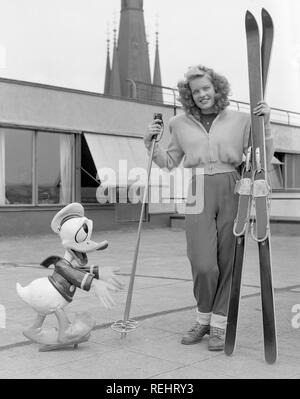 Wintersport in den 1950er Jahren. Eine junge blonde Frau mit ihrem Ski, Stöcke und Schuhe zusammen mit einem Donald Duck Figur. Schweden 1952. Foto Kristoffersson Ref 179 A-1 Stockfoto