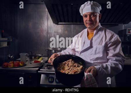 Küchenchef, tolles Design für irgendwelche Zwecke. Kochen Konzept. Küche Porträt. Gesundes Essen. Diät Konzept. Koch Konzept. Professioneller Koch Mann. Dunkle bac Stockfoto