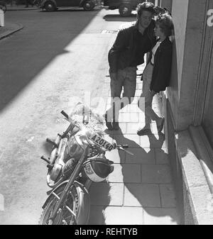 Paare, die in den 1950er Jahren. Ein junges Paar steht lehnte sich an eine Hauswand in einer Stockholmer Straße. Er hat einen Triumph Motorrad neben mit einer typischen Kammgarn gepolsterte Sitz geparkt. Foto Kristoffersson ref CA 29-10. Schweden 1958 Stockfoto