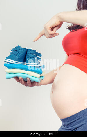 Schwangere Frau, die Kleidung für Baby, Konzept der Familie erweitern und erwartet für Neugeborene Stockfoto