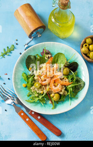 Diätmenü, veganes Essen. Gesunde Salate mit Quinoa, Rucola, Garnelen und Oliven auf einem blauen Tisch aus Stein. Stockfoto