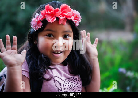 Eine hübsche junge native suchen Mädchen mit einem Rucksack und floralen Kopf band mit den Händen in der Luft, ein Gefühl zum Ausdruck der Überraschung. Stockfoto